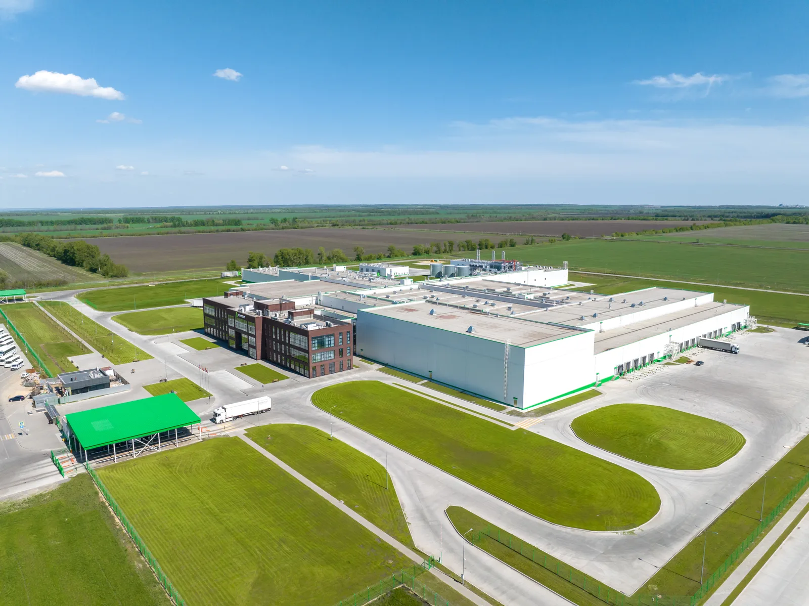 Vista aérea de una planta agroindustrial moderna de naves blancas, rodeada de campo abierto.